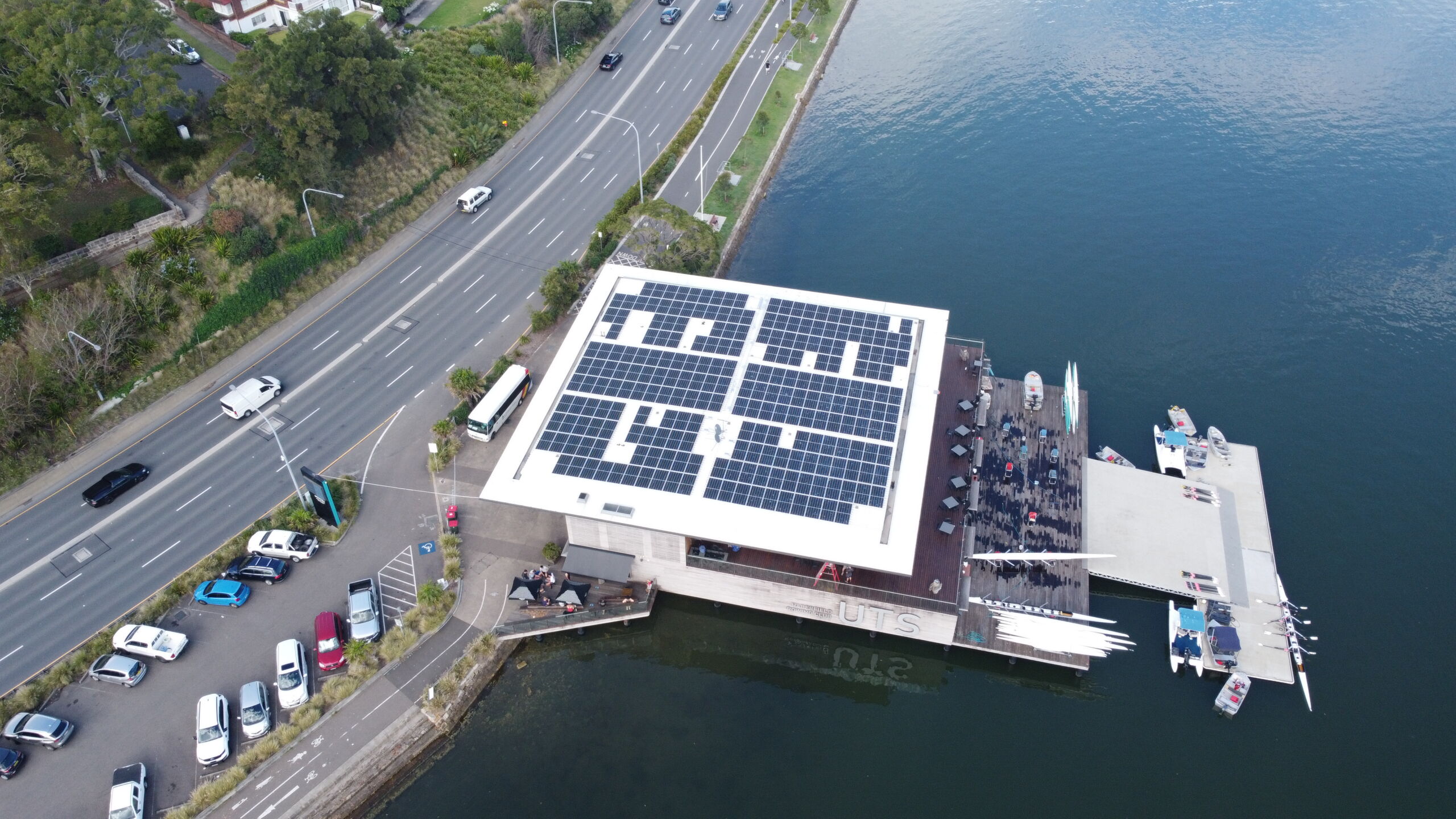 This image shows solar panels on top of a UTS building that is situated on a lake.